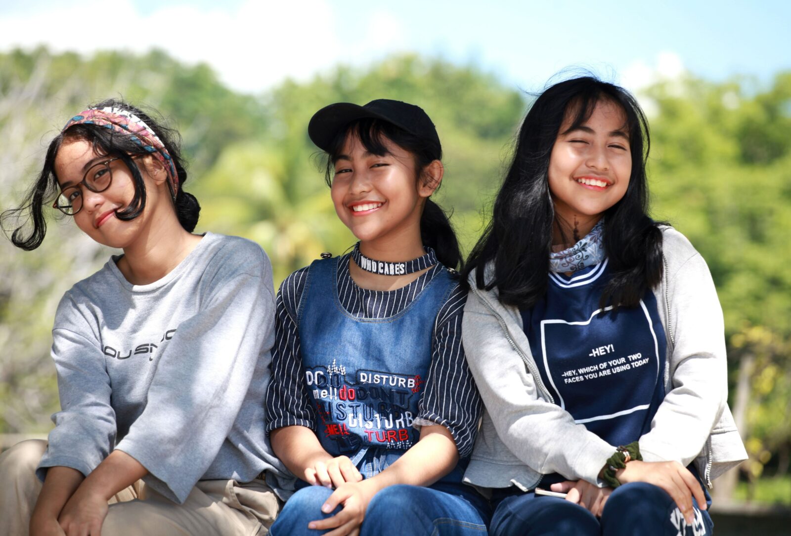 Three pre-teen girls sitting together smiling in a park